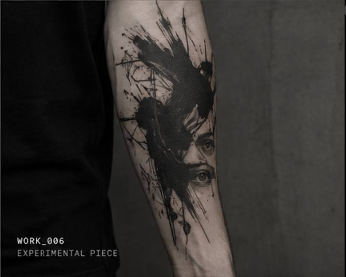 Bold black ink abstract tattoo with an eye motif, forearm